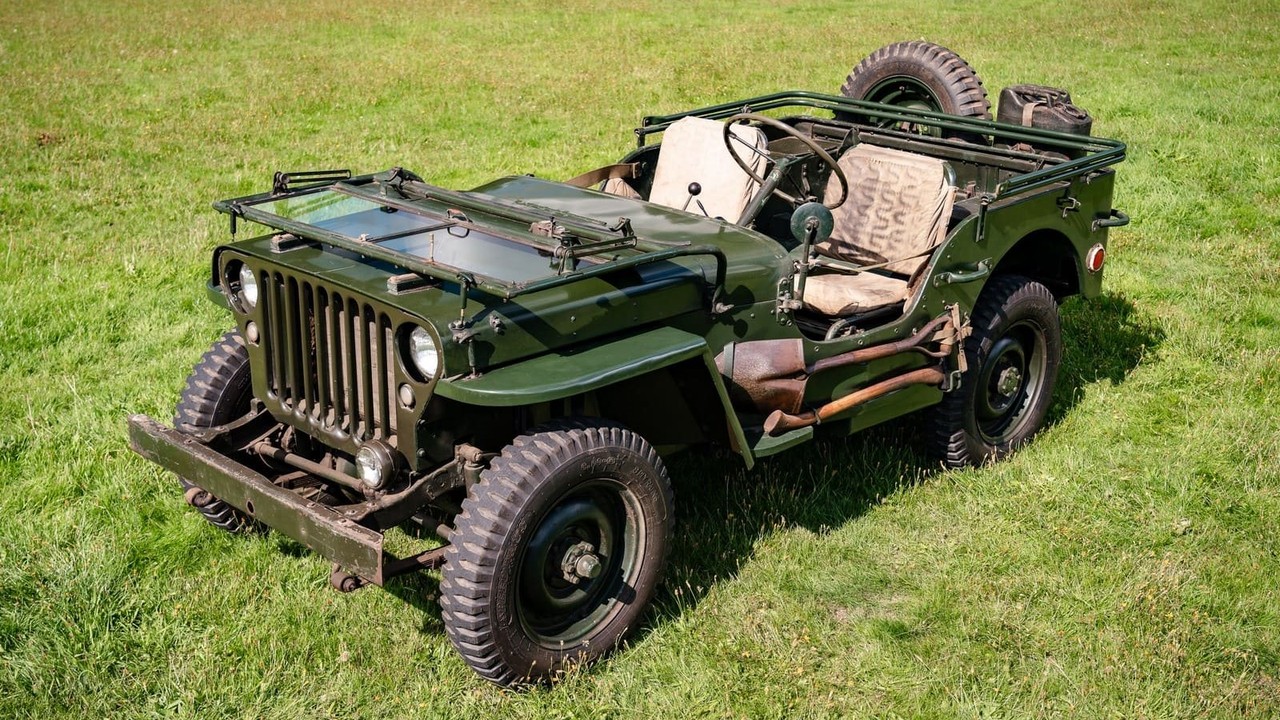 हरे मैदान में खड़ी सैन्य हरे रंग की क्लासिक Jeep Willys MB का फ्रंट थ्री-क्वार्टर व्यू